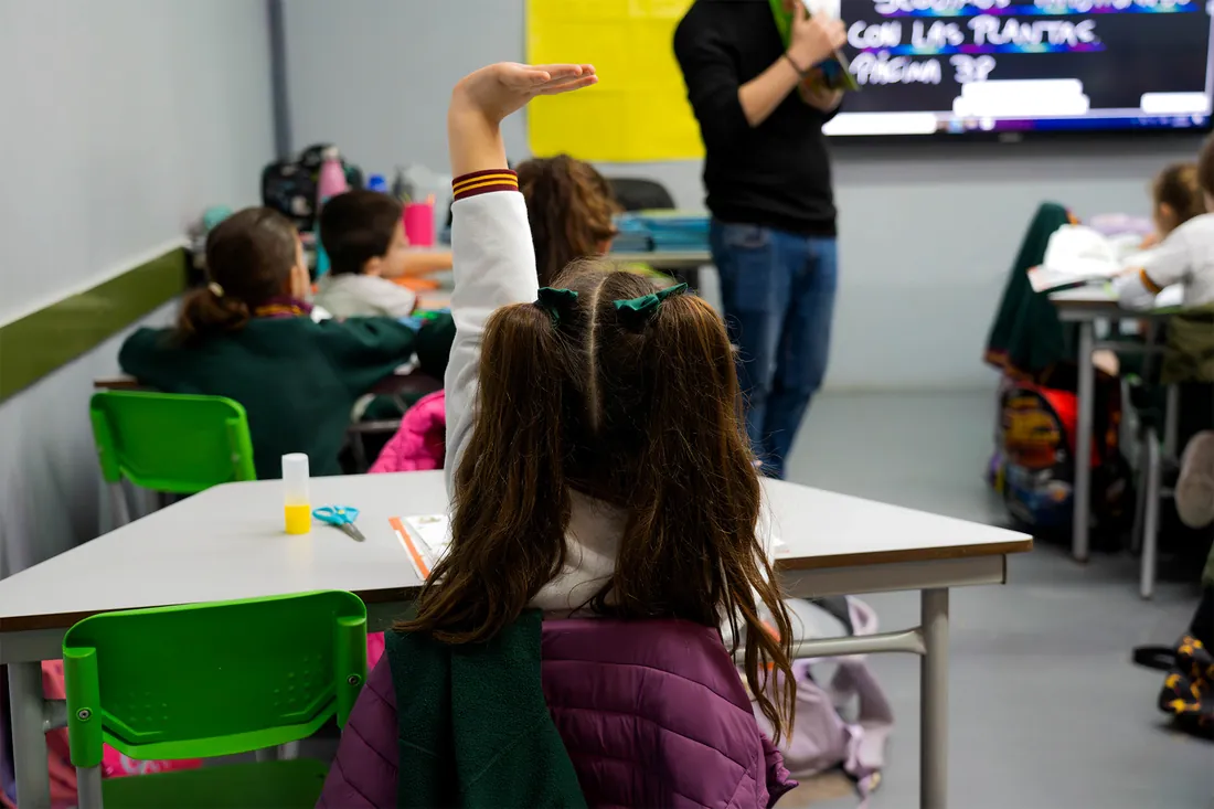 Maestra al frente de un aula del Nivel Primario del IESM mientras varios alumnos levantan la mano